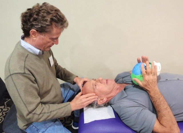 A CFR practitioner performing the nasal release technique on a patient at a seminar, model skull in hand