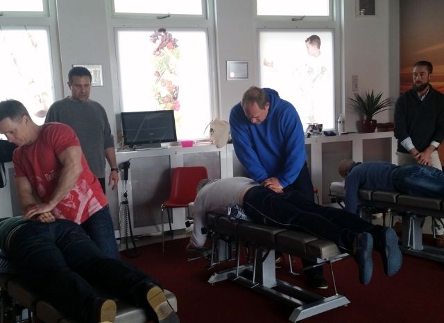 Doctors practicing Cranial Facial Release on patients lying on treatment tables in a seminar room
